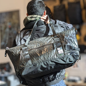 Person carrying a large black duffel bag in a crinkly xpac material.