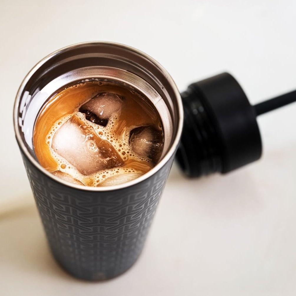 Black insulated tumbler with iced coffee on a light background